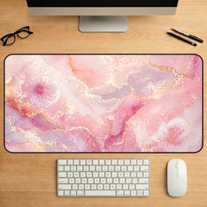 May include: A rectangular mouse pad with a pink, white, and gold marble design. The pad is surrounded by a black border and sits on a wooden desk. A keyboard, mouse, monitor, and glasses are also visible.