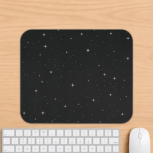 May include: A rectangular mouse pad featuring a black background with a repeating pattern of white four-pointed stars of varying sizes, creating a celestial night sky effect across the entire surface of the computer accessory.