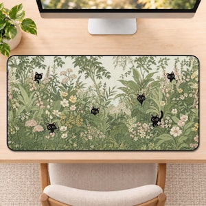 May include: A rectangular desk mat featuring a detailed illustration of a lush garden filled with various green plants, foliage, and small white and yellow flowers. Five small black cats with large eyes are peeking out from the dense greenery.