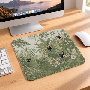 May include: A rectangular mouse pad featuring a botanical illustration of dense green foliage, various small white and pink flowers, and three small black cats peeking out from within the lush garden plants and leaves.