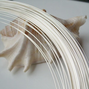 May include: A coil of thin, bright silver-colored wire arranged in a circular pattern. The wire has a smooth, reflective metallic surface and is composed of multiple individual strands bundled together to form a continuous, uniform loop.
