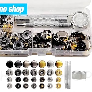 Könnte beinhalten: Eine transparente Kunststoff-Organizer-Box gefüllt mit verschiedenen Metall-Druckknöpfen in Silber-, Schwarz- und Goldtönen. Enthält Werkzeuge zum Anbringen von Druckknöpfen. Die Box trägt den Text "Hamo shop" in einem blauen Banner.