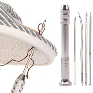 May include: A shoe being repaired with a silver needle and brown thread. A silver needle holder and several needles are displayed to the right. The shoe is white with a green and white striped pattern.