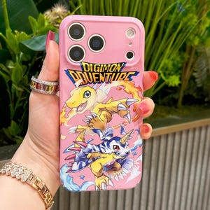 May include: Pink phone case featuring the text "DIGIMON ADVENTURE" and illustrations of Digimon characters. The case has a glossy finish and cutouts for the camera and buttons.