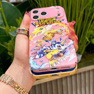 May include: Pink phone case featuring a colorful Digimon Adventure design. The case has a yellow and blue border and a vibrant graphic of Digimon characters. The text "DIGIMON ADVENTURE" is displayed at the top.