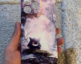 May include: A purple phone case featuring a winter forest scene with a Gengar character. The case has a glossy finish and cutouts for the camera and buttons. The Gengar is black with a sinister grin and red eyes.