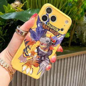 May include: Yellow phone case featuring a Digimon Adventure graphic. The case has a cartoon image of a monster with orange, blue, and gray colors. The text "DIGIMON ADVENTURE" is printed on the case in blue and white.