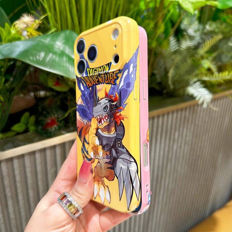 May include: Yellow and pink phone case featuring a Digimon Adventure graphic. The case has a cartoon illustration of a Digimon character with the text "DIGIMON ADVENTURE". The case is designed to protect the phone.