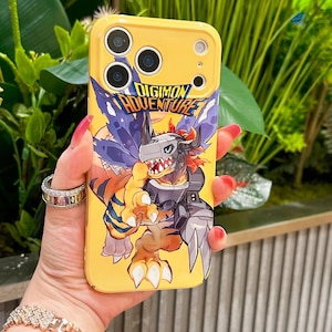 May include: Yellow phone case featuring a Digimon Adventure graphic. The case has a cartoon illustration of a monster with orange, gray, and blue colors. The text "DIGIMON ADVENTURE" is displayed in a blue and white font.