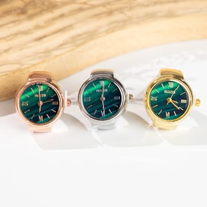 May include: Three ring watches with green watch faces and gold, silver, and rose gold bands. The watch faces have Roman numerals and the brand name "BOZI". The watches are displayed on a white surface.