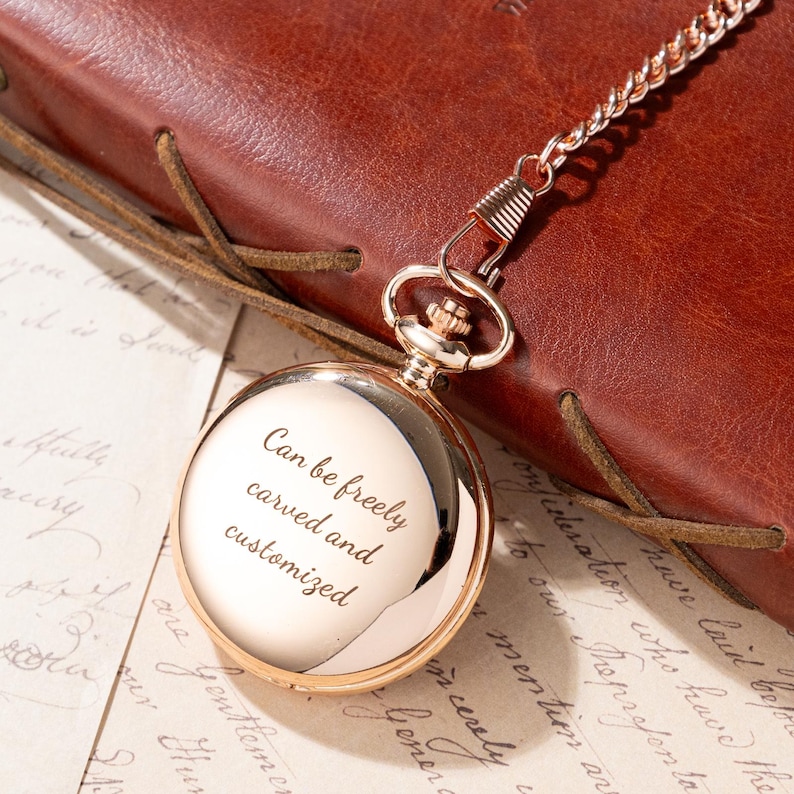 Puede incluir: Un reloj de bolsillo dorado con cadena, sobre una superficie de cuero marr&oacute;n. La esfera del reloj es reflectante, con el texto "Can be freely carved and customized" grabado. Un accesorio cl&aacute;sico.