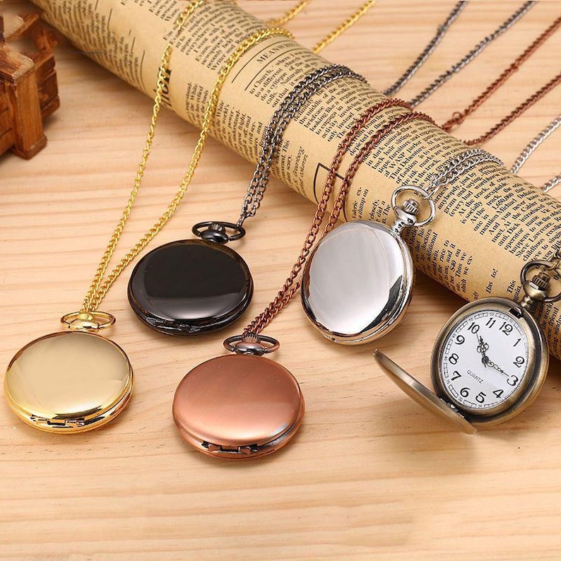 Puede incluir: Una colecci&oacute;n de relojes de bolsillo de estilo antiguo con varios acabados, incluyendo oro, negro, plata y cobre. Cada reloj est&aacute; suspendido de una cadena a juego. Un reloj est&aacute; abierto, revelando una esfera blanca con n&uacute;meros negros.