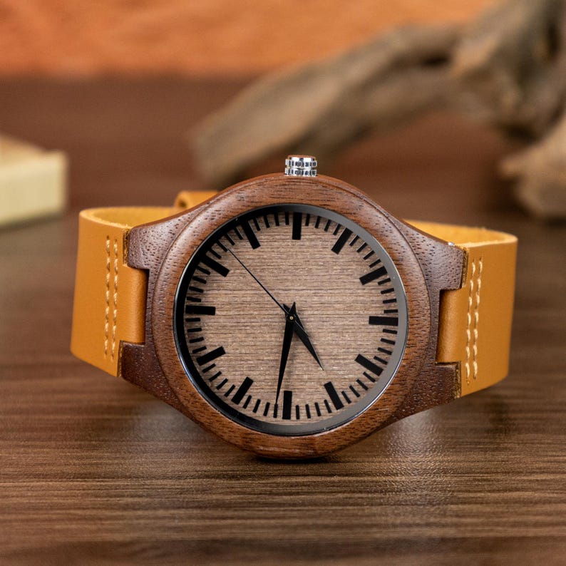 Puede incluir: Un reloj de pulsera de madera con esfera marr&oacute;n claro y bisel marr&oacute;n oscuro. El reloj tiene una correa de cuero marr&oacute;n claro. La esfera del reloj presenta marcadores de hora y agujas negras. El reloj se muestra sobre una superficie de madera.