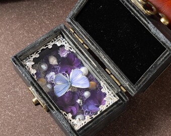 Caja de tesoros de madera antigua, joyero con ejemplar de mariposa azul auténtica, recuerdo de baratija con flor púrpura preservada.