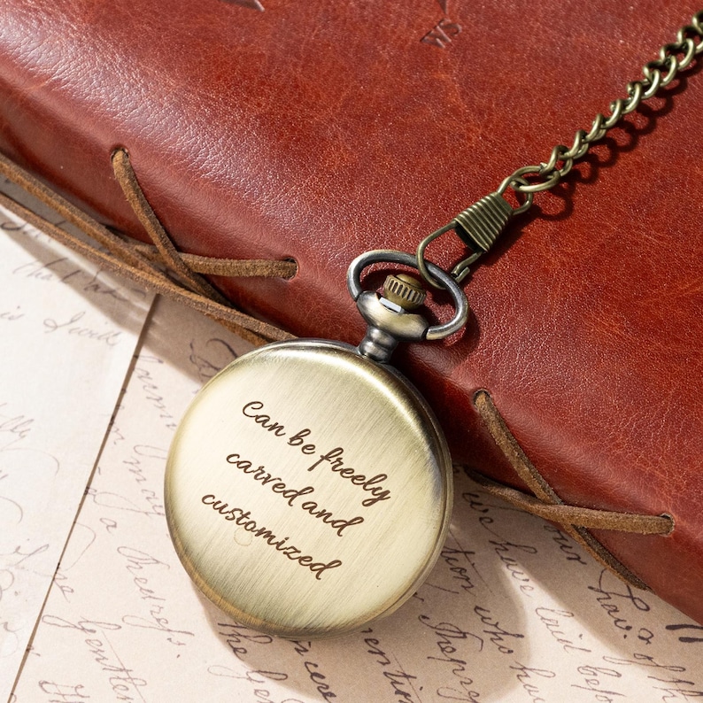 Puede incluir: Un reloj de bolsillo de bronce con cadena. La esfera del reloj tiene el texto "Can be freely carved and customized". El reloj descansa sobre un papel con texto manuscrito, junto a un diario de cuero marr&oacute;n. Dise&ntilde;o cl&aacute;sico.