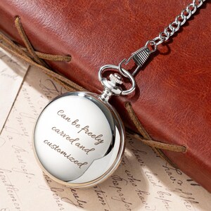 Puede incluir: Un reloj de bolsillo plateado con una cadena, apoyado sobre una superficie de cuero marr&oacute;n. La esfera del reloj tiene el texto "Can be freely carved and customized". El reloj es redondo y tiene una superficie brillante y reflectante.