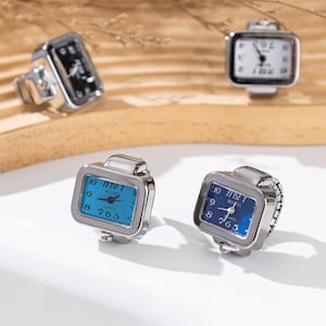 May include: Silver-toned ring watches with square faces. The watch faces display the time with black numerals on a white, blue, and black background. The watch bands are silver and adjustable. The watches are quartz.