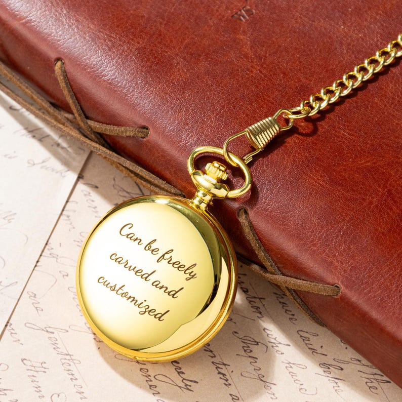 Puede incluir: Un reloj de bolsillo dorado con cadena, apoyado en un diario de cuero marr&oacute;n. La esfera del reloj tiene el texto grabado: "Can be freely carved and customized". El reloj es redondo y tiene un acabado pulido.
