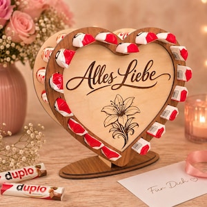 May include: A wooden heart-shaped candy display with the words "Alles Liebe" and a floral design. The display holds numerous red and white wrapped candies. A card with the words "Für Dich" is also visible.