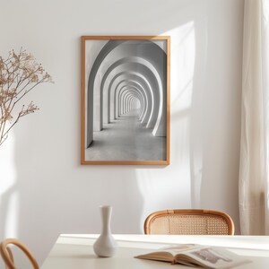 May include: A framed print featuring a grayscale image of a long hallway with repeating archways. The artwork is in a light brown wooden frame and hangs on a white wall. The scene evokes a sense of depth and perspective.
