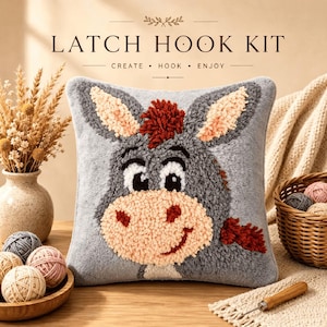 Peut inclure: Un coussin carré de kit de crochet à loquet représentant un âne gris avec un museau pêche, des cheveux rouge foncé et de grands yeux. Le texte LATCH HOOK KIT CREATE HOOK ENJOY est imprimé au-dessus. Le motif est texturé avec des boucles de laine.