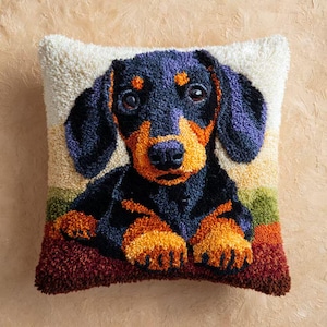 Könnte beinhalten: Ein quadratisches Zierkissen mit einem detaillierten Bild eines Dackelhundes. Der Hund hat schwarzes, orangefarbenes und violettes Fell, vor einem cremefarbenen Hintergrund. Das Kissen hat ein gestreiftes Muster in Grün, Gelb und Rot.