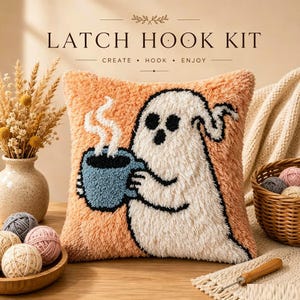 May include: A square latch hook kit cushion featuring a white ghost holding a blue mug with rising steam against an orange background. The text LATCH HOOK KIT CREATE HOOK ENJOY is printed above the cushion. The design is textured and fuzzy.