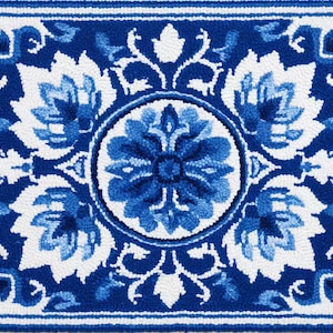May include: A rectangular rug featuring a punch needle texture with a symmetrical floral pattern in shades of deep blue, light blue, and white. The design includes a central circular medallion surrounded by four large stylized flower motifs.