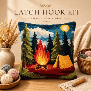 May include: A latch hook kit featuring a square cushion with a textured design of a campfire, a yellow tent, and dark green pine trees under a blue sky with a yellow sun. The text LATCH HOOK KIT CREATE HOOK ENJOY is printed above the cushion.