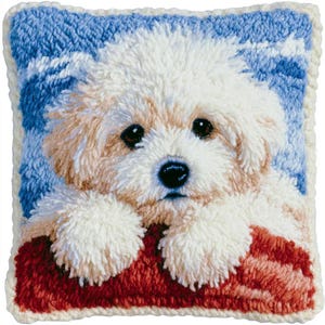 May include: A square throw pillow featuring a textured punch needle design of a fluffy white puppy with light tan ears. The puppy rests its paws on a dark red surface against a blue and white sky background, finished with a cream-colored border.