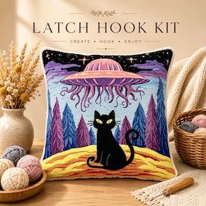 May include: A square latch hook kit pillow featuring a black cat sitting on a yellow landscape under a purple UFO and a dark starry sky with blue and purple trees. The text LATCH HOOK KIT CREATE HOOK ENJOY is printed above the pillow.