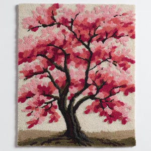 May include: A hand-tufted wall hanging featuring a stylized cherry blossom tree. The tree has a dark brown trunk and branches, with vibrant pink and red blossoms. The background is a neutral beige, and the base is a darker brown.