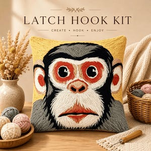 May include: A square latch hook kit pillow featuring a stylized monkey face with black, white, gray, and orange yarn embroidery on a yellow background. The text LATCH HOOK KIT CREATE HOOK ENJOY is printed above the pillow in a dark brown font.