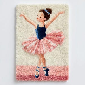 Puede incluir: Una alfombra hecha a mano que representa a una bailarina con un maillot azul y un tutú rosa. La bailarina tiene los brazos extendidos y su cabello está peinado en un moño con un lazo azul. La alfombra tiene un fondo crema con un borde rosa.
