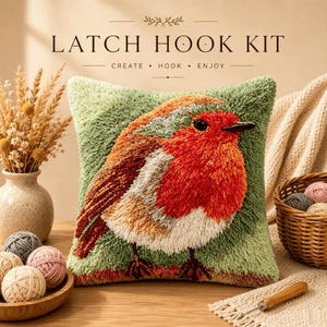 May include: A square latch hook kit pillow featuring a textured robin bird design with orange, red, and white yarn on a sage green background. The text LATCH HOOK KIT CREATE • HOOK • ENJOY is printed above the pillow. The pillow is surrounded by yarn.