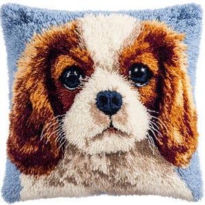 May include: A square scatter cushion featuring a textured latch hook design of a Cavalier King Charles Spaniel dog face. The dog has long brown and white ears, a white muzzle, and dark eyes against a light blue background with a soft pile finish.