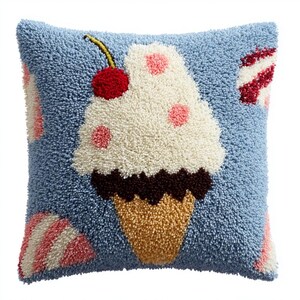 May include: A square throw pillow with a textured punch needle design on a light blue background. The central motif is a white ice cream cone with pink polka dots, a dark brown chocolate layer, and a bright red cherry on top.