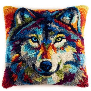 Könnte beinhalten: Ein quadratisches Zierkissen mit einem farbenfrohen Punch-Needle-Design eines Wolfsgesichts. Der Wolf ist in Blau-, Orange-, Gelb-, Lila- und Weißtönen gehalten, wobei ein Auge blau und das andere gelb ist, eingebettet in einen strukturierten Hintergrund.
