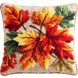 Peut inclure: Un coussin carré avec une surface texturée en laine bouclée représentant un motif central de feuilles d'érable automnales aux teintes vives de rouge, orange, jaune et vert sur un fond crème avec un bord passepoilé assorti.