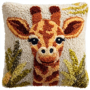 Könnte beinhalten: Ein quadratisches, cremefarbenes Kissen mit einem detaillierten, strukturierten Design eines Giraffengesichts. Die Giraffe hat braune und orangefarbene Flecken, große schwarze Augen und einen lächelnden Ausdruck. Grüne und gelbe Blätter akzentuieren die Seiten.