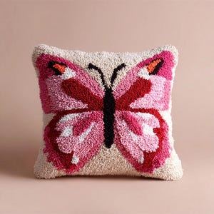 May include: A square scatter cushion featuring a textured punch needle design of a butterfly. The butterfly has a black body and wings in shades of pink, red, white, and orange, set against a cream-coloured background with a looped yarn texture.