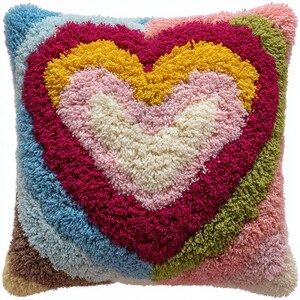 Könnte beinhalten: Quadratisches Zierkissen mit Herzmuster. Das Herz besteht aus strukturiertem, farbenfrohem Garn in Weiß-, Rosa-, Gelb- und Rottönen. Der Hintergrund ist eine Mischung aus Blau, Grün und Braun.