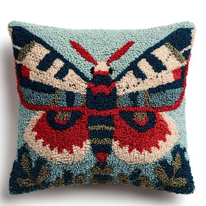 Peut inclure: Coussin carré avec un fond bleu clair texturé. Le coussin présente un grand motif de papillon de nuit coloré en rouge, bleu marine et beige. Les ailes du papillon de nuit sont ornées de motifs géométriques, et le style général rappelle l'art populaire.