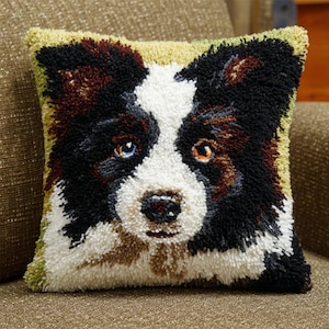 Op de afbeelding: Vierkant decoratief kussen met een gedetailleerde, getextureerde afbeelding van een hondengezicht. De hond heeft zwart, wit en bruin haar, met één blauw en één oranje oog. Het kussen heeft een lichtgroene rand en ligt op een bruin oppervlak.