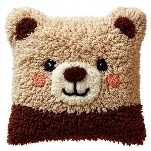 Könnte beinhalten: Ein quadratisches, weiches Kissen mit einem Teddybären-Design. Das Kissen hat einen hellbraunen Hintergrund mit einem dunkleren braunen Rand und Akzenten. Das Gesicht des Bären hat eine weiße Schnauze, eine dunkelbraune Nase, schwarze Augen und rosa Wangen.