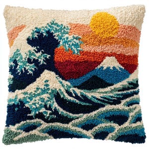 May include: A square throw pillow featuring a textured punch needle design of a large ocean wave, a mountain peak, and a vibrant sunset. The scene uses a palette of navy blue, teal, white, orange, pink, and yellow yarn to create a detailed landscape.
