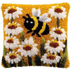 May include: A square, yellow decorative pillow with a textured surface. The pillow features a design of white daisies with brown centers, green foliage, and a black and yellow bee. The pillow is a home decor item.