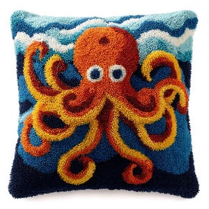 Può includere: Un cuscino quadrato con un design testurizzato a punch needle che raffigura un polpo arancione brillante con tentacoli dalle punte gialle. Il polpo è centrato su uno sfondo di profondità blu scuro e onde stilizzate blu chiaro e bianche.