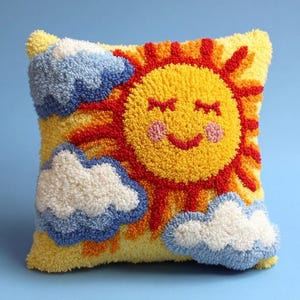 May include: A square throw pillow featuring a textured punch needle design of a smiling yellow sun with pink cheeks and red rays. The background is yellow with three fluffy clouds in shades of white and light blue, creating a tactile surface.