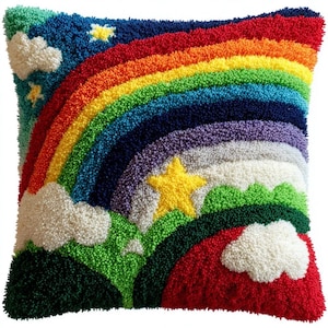 Peut inclure: Un coussin carré avec un motif en punch needle texturé représentant un arc-en-ciel vibrant sur un ciel bleu foncé. La scène comprend des nuages blancs, des étoiles jaune vif et des collines vertes à la base, le tout réalisé en laine.